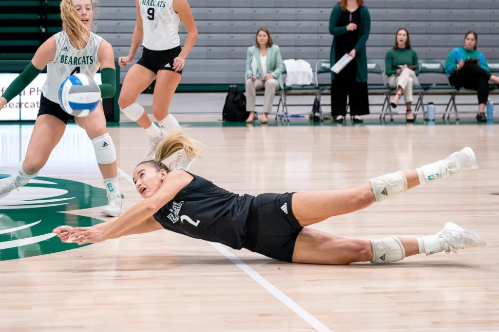 A college volleyball player dives and bumps the ball into the air.